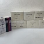 バッハ大全集の白い箱7つが2段に積まれ、左に解説書6冊と紺色の第1巻が並ぶ