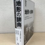 地形の辞典の白いカバーにDictionary of Landformsの英題と日本地形学連合の記章が入り、背に責任編集の3人の名前が並んでいる