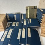 複刻日本古典文学館の紺の和装本が積まれ、画本虫撰や好色一代男、里見八犬伝の題簽と桐箱、解題の冊子が並んでいる