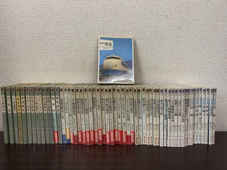 保育社カラーブックスの鉄道の巻56冊が背を見せて横一列に並び、上に0系新幹線の表紙の日本の鉄道が立っている