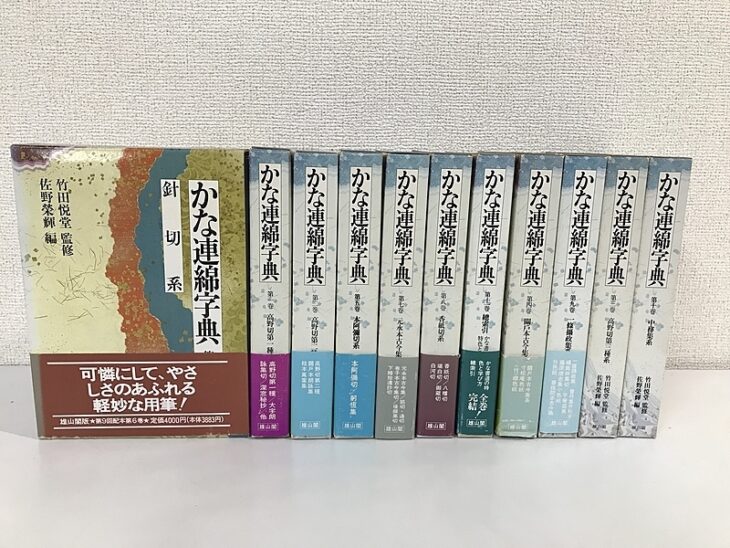 代替テキスト かな連綿字典と背に入った函が11冊並び、系統名と配本の帯が付いたところ
