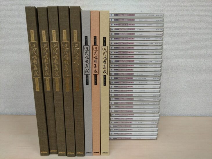 原典による近代唱歌集成の茶色い函5冊と演奏用楽譜3冊、右にCD30枚が背を見せて並ぶ