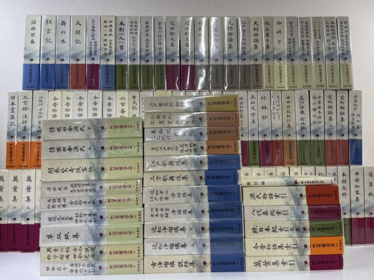 新日本古典文学大系の色分けされた函が三段に並び、謡曲百番や太閤記、萬葉集などの巻名が背に入っている