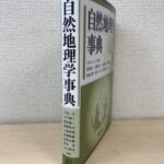 自然地理学事典の白い背に小池一之から山川修治まで9人の編集者名が並び、カバーに地球の地図があしらわれている