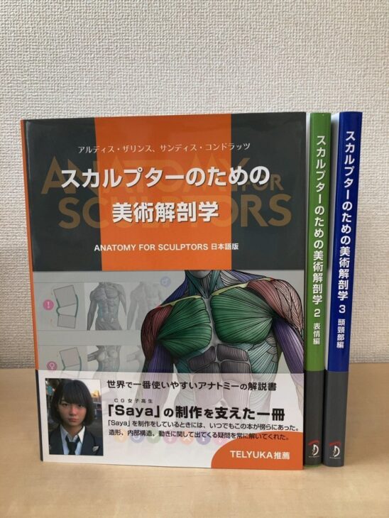 スカルプターのための美術解剖学の1巻を手前に置き、緑の背の2 表情編と青の背の3 頭頸部編を立てた3冊。1巻にはSayaの帯がついている