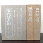 謙光社『現代易占術』改訂増補版の函3つ。左の函の表はひび割れ模様の地に銀の文字で書名と「加藤大岳監修」「全三巻 改訂増補」、右の2つは中巻と下巻の背で下に謙光社