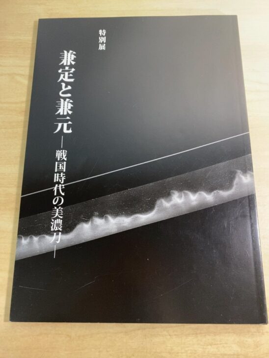 特別展『兼定と兼元 戦国時代の美濃刀』の黒い表紙と、刃文が浮かぶ刀身の写真