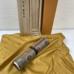 蓋に宋 米芾 蜀素帖と墨書された桐箱と橙色の外箱、黄色い布の上に置いた錦の表紙の巻子