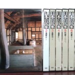 囲炉裏と太い曲がった柱の写真が函に入った学研『日本の民家』第1巻と、背を向けた第2巻から第8巻