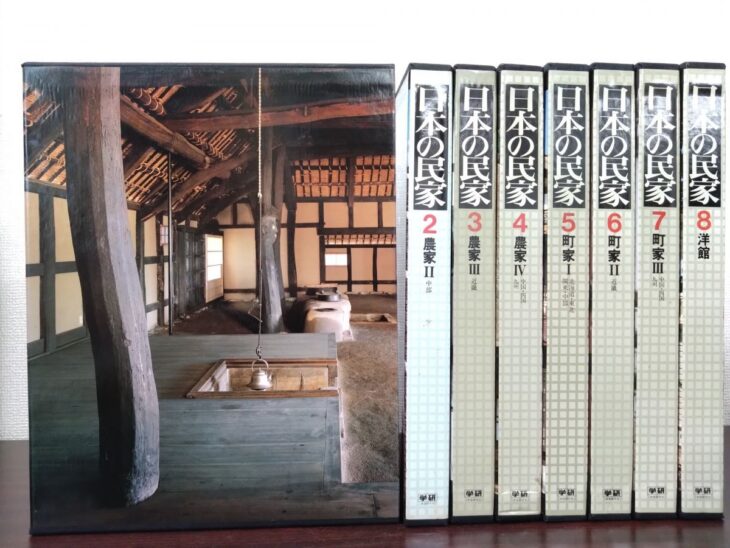 囲炉裏と太い曲がった柱の写真が函に入った学研『日本の民家』第1巻と、背を向けた第2巻から第8巻