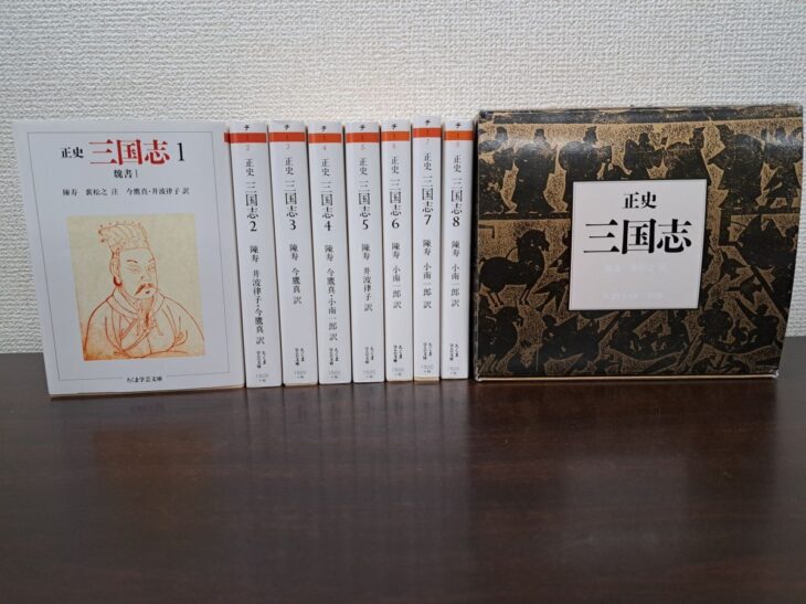 ちくま学芸文庫『正史 三国志』8冊と外箱。左端の第1巻は表紙に朱色の線の人物画と「魏書I」、第2巻から第8巻は背に巻数と訳者名、右に黒と茶色で馬や人を描いた箱