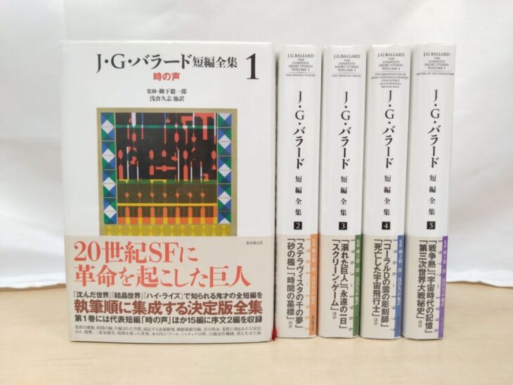 東京創元社『J・G・バラード短編全集』の5冊。左の第1巻は表に赤い「時の声」と四角い装画、赤い大きな字の帯。右の4冊は背に英語の全集名と表題作の題、帯に橙、緑、青、紫の縦の線