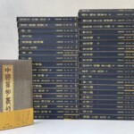 紺色の中国篆刻叢刊の函が2列に積まれ、背に金の字で文彭 何震 丁敬 呉昌碩 齊白石などの印人名と巻数。左手前に第1巻の表