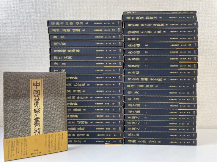 紺色の中国篆刻叢刊の函が2列に積まれ、背に金の字で文彭 何震 丁敬 呉昌碩 齊白石などの印人名と巻数。左手前に第1巻の表