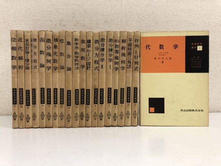 黒い布装の基礎数学講座が20冊並び、背に金の字で位相数学 近代解析 函数論 微分幾何学 整数論 集合論などの題と番号。右に第1巻 代数学の表紙
