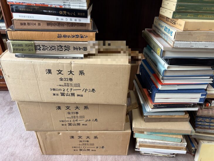 冨山房『漢文大系』全22巻の箱3つの上に『中國石窟 敦煌莫高窟』や奈良国立博物館の図録が積まれ、右に東洋文庫などの本の山が続く部屋の隅