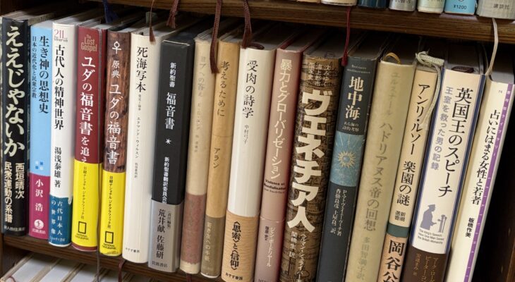 木の本棚の別の段。西垣晴次『ええじゃないか』、湯浅泰雄『古代人の精神世界』、『新約聖書 福音書』、中村弓子『受肉の詩学』、ボードリヤール『暴力とグローバリゼーション』、岡谷公二『アンリ・ルソー 楽園の謎』、『英国王のスピーチ』の背