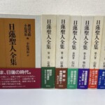 日蓮聖人全集の白い函7冊。左の第1巻は表に茶色の題簽と「いま、日蓮の時代。」の赤い帯、右の6冊は背に巻数と宗義 信行 聖伝 信徒の巻名