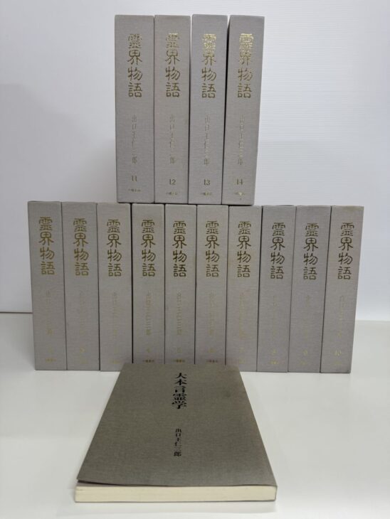 灰色の布装の霊界物語が2段に並び、背に金の字で霊界物語 出口王仁三郎と1から14の番号。手前に大本言霊学の薄い1冊