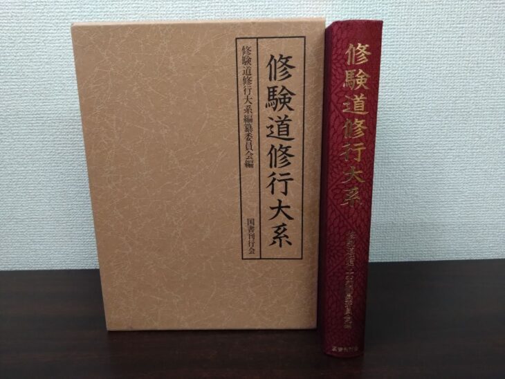 黒い枠に書名を入れた茶色い紙の函と、えんじ色の布の背に金文字で修験道修行大系と入った本体1冊