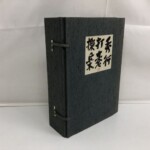 濃い灰色の布を張った帙の表と、筆書きで秀行打碁撰集と入った生成り色の題簽、横の面の骨色の爪