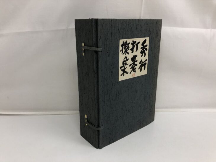 濃い灰色の布を張った帙の表と、筆書きで秀行打碁撰集と入った生成り色の題簽、横の面の骨色の爪