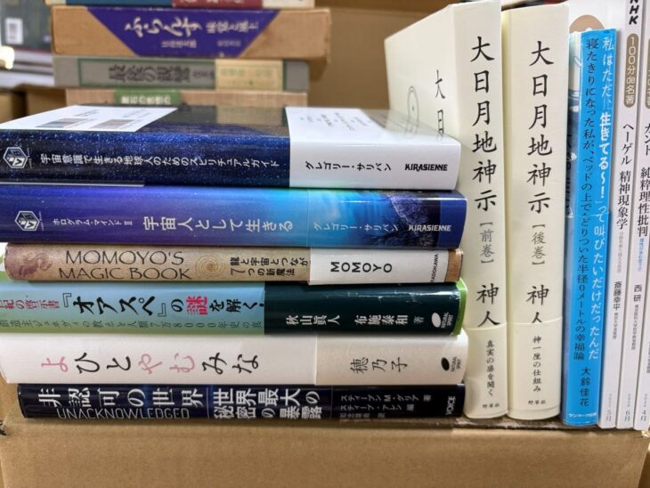 段ボールに詰めた精神世界の本。左に『宇宙意識で生きる地球人のためのスピリチュアルガイド』『宇宙人として生きる』『よひとやむみな』の背、右に神人『大日月地神示』前巻と後巻