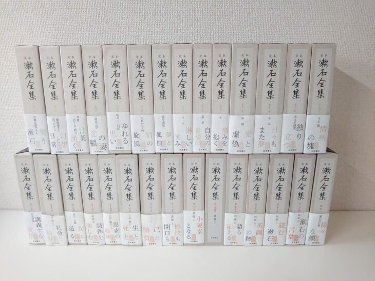 定本漱石全集の白い函29冊が2段に並び、背に定本の文字と漱石全集の題、帯に笑う日常 幻想と漱石 情熱の塊などの文句