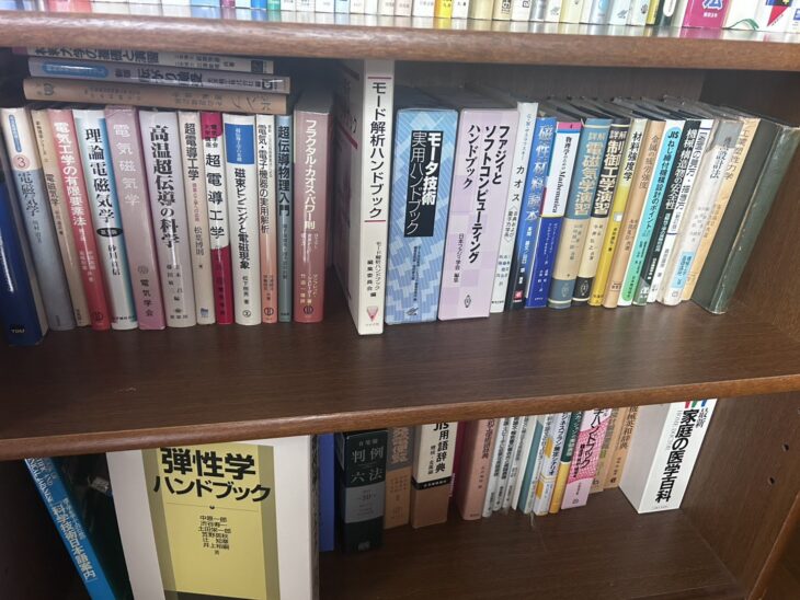 木の本棚。『理論電磁気学』『高温超伝導の科学』『超電導工学』『磁束ピンニングと電磁現象』『モード解析ハンドブック』『モータ技術実用ハンドブック』、下の段に『弾性学ハンドブック』