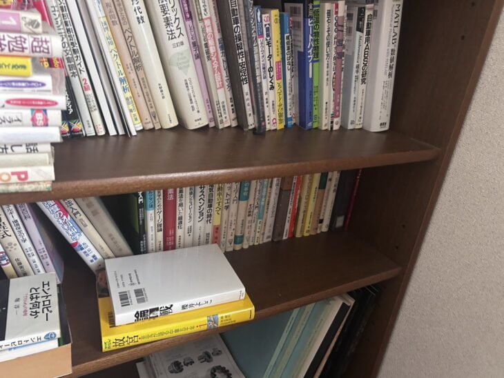 本棚の2段。『自動車の操縦性・安定性』『自動車用ABSの研究』『MATLABによる数値解析』『磁石とその使い方』、下の段に『電気自動車の時代』『サスペンション』『ロボット工学』